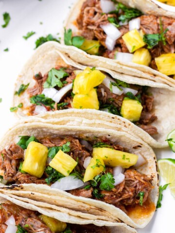 Four Tacos with Al Pastor Meat and Diced Pineapple Stacked in a Row