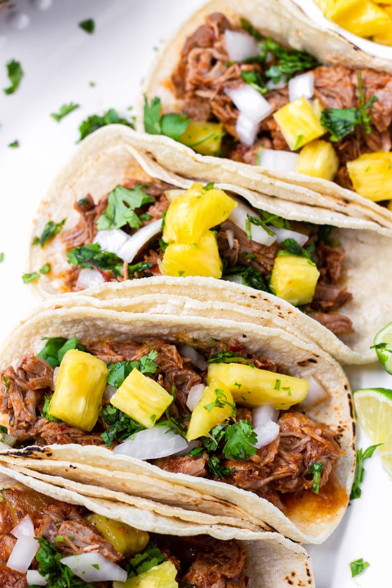 Four Tacos with Al Pastor Meat and Diced Pineapple Stacked in a Row