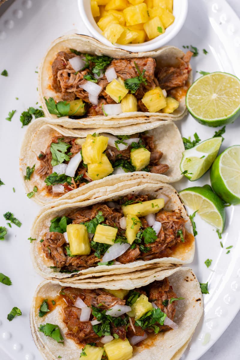 Top view of four pork tacos topped with pineapples, cilantro, and onions