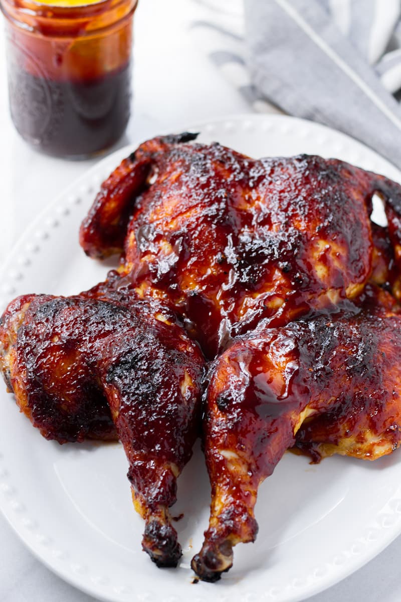 A butterflied chicken with BBQ sauce on a white plate