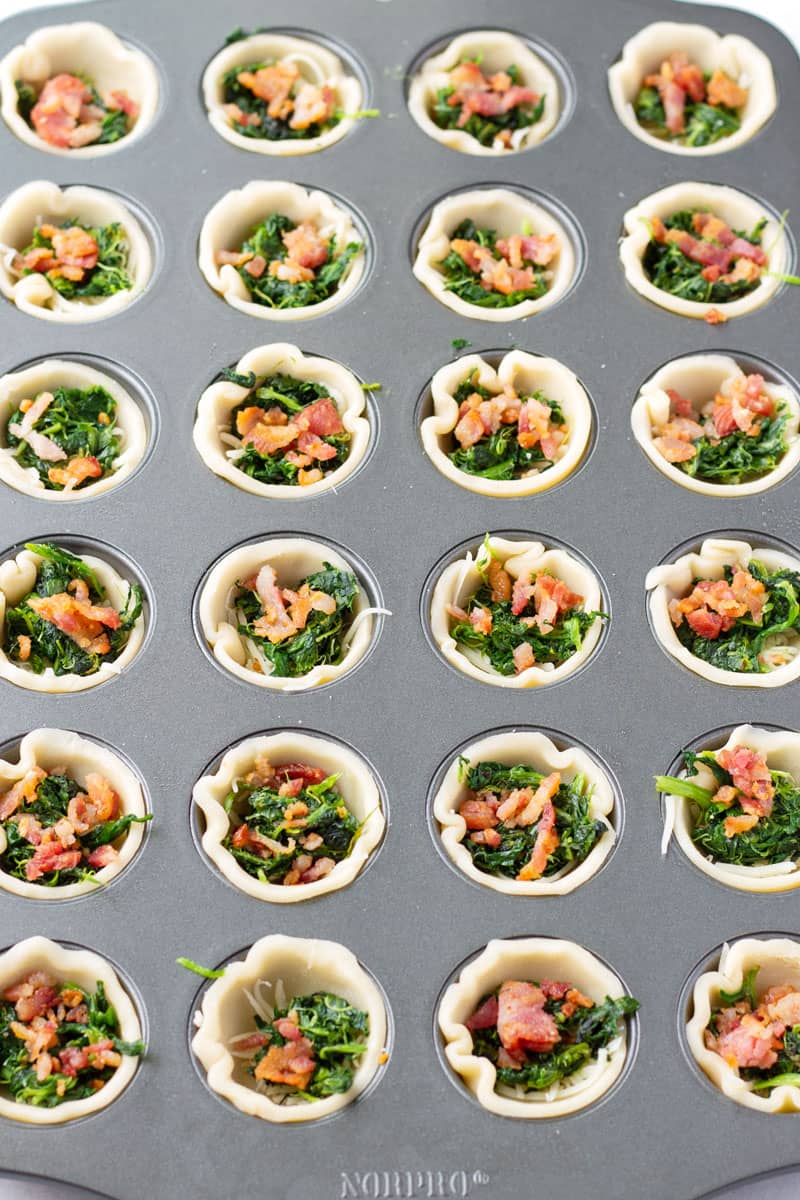Mini muffin tin filled with pie dough, spinach, bacon
