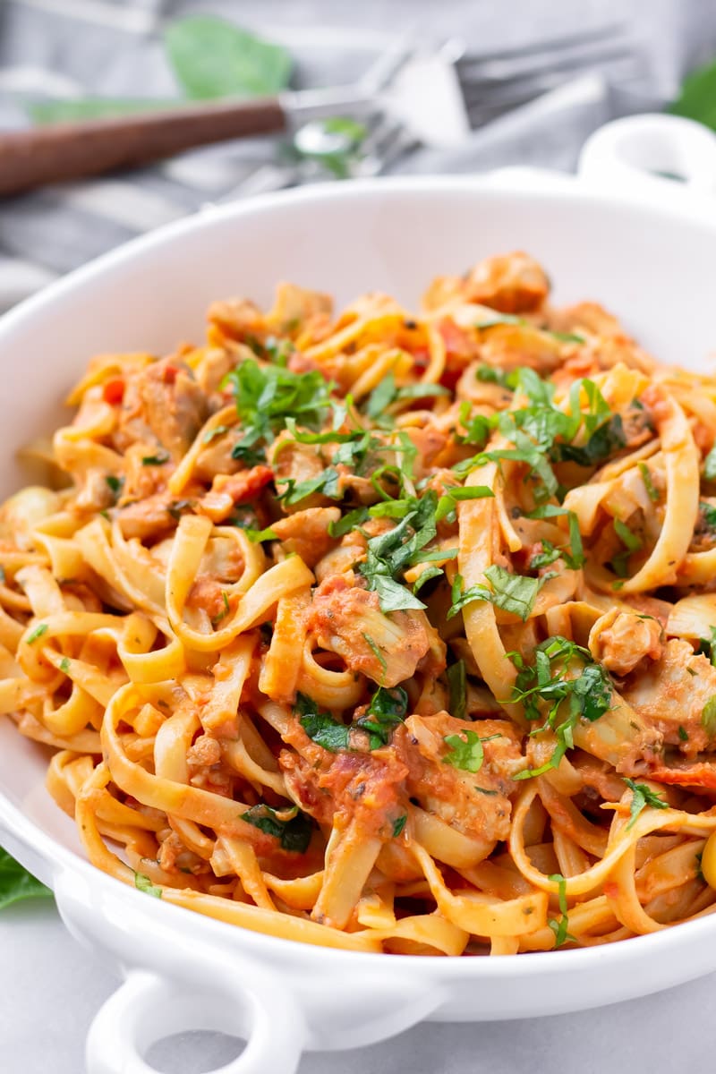 Chicken artichoke pasta with creamy tomato sauce and basil garnish on white bowl