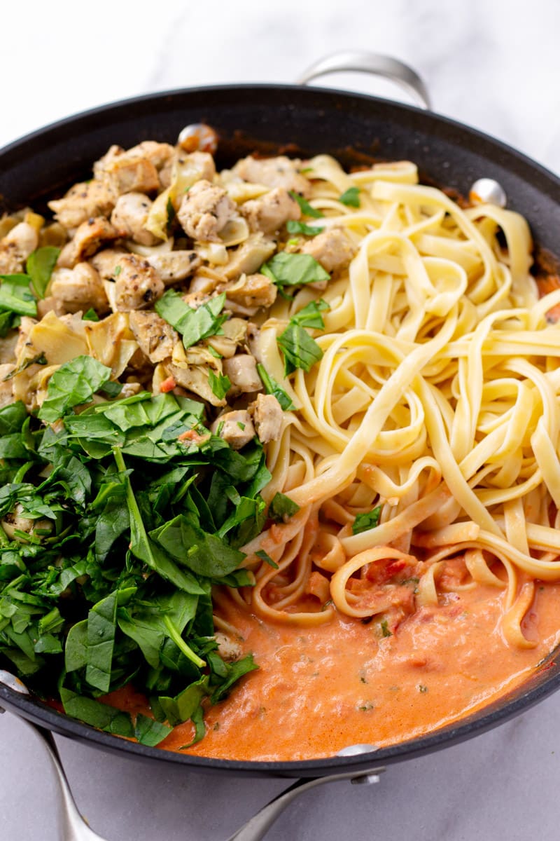 Skillet with ingredients side by side, spinach, chicken, artichokes, pasta, and creamy tomato sauce