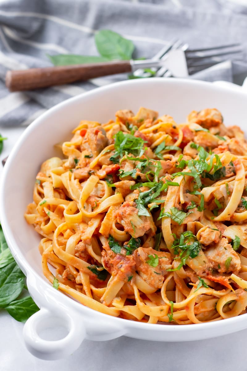 White shallow bowl with fettuccine tossed with sauteed chicken, artichokes, and spinach