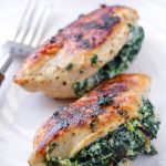 Two pan-seared chicken breasts stuffed with spinach and ricotta on a white plate
