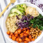 Roasted sweet potatoes, kale, quinoa, avocado served on while bowl and golden fork