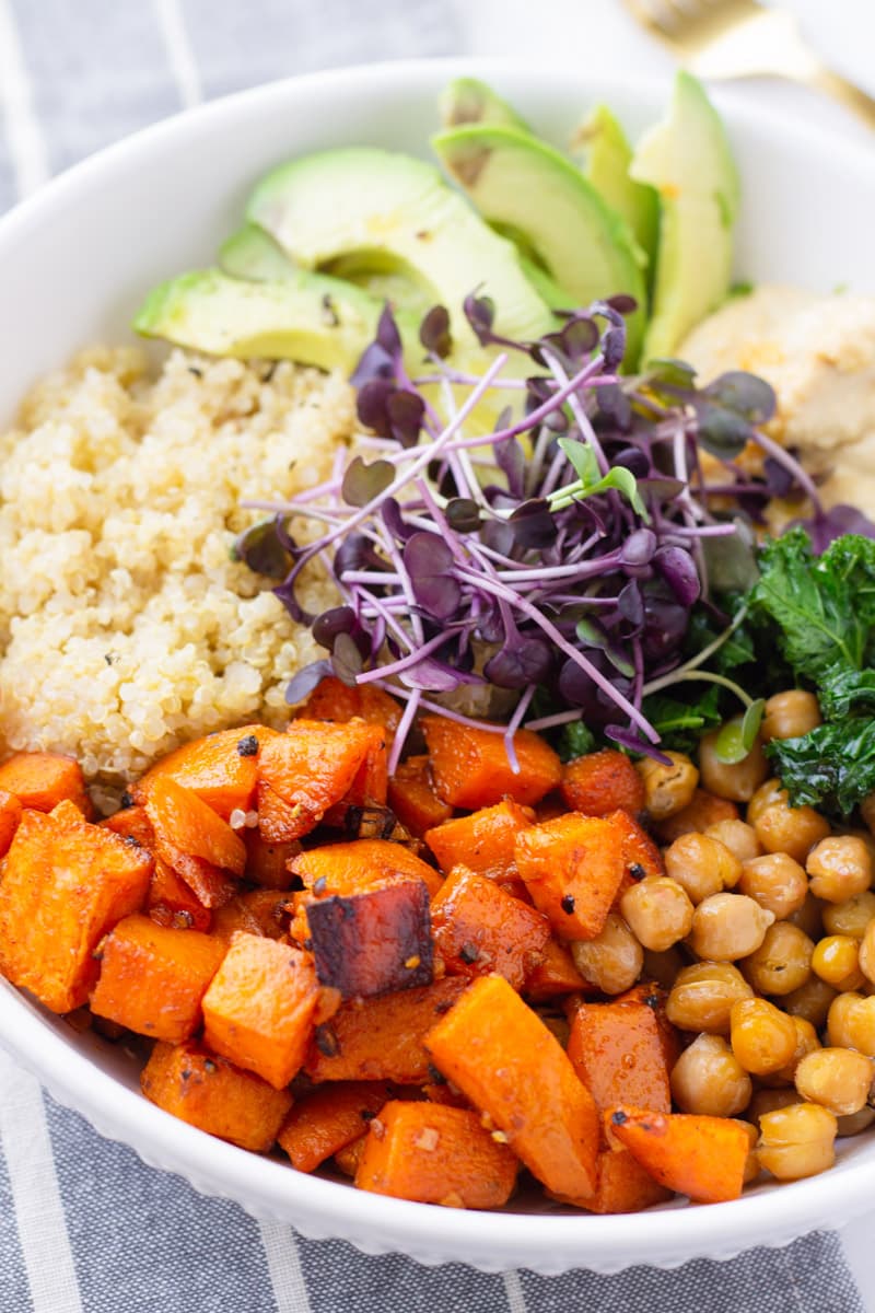close up of white bowl with roasted sweet potatoes, quinoa, and microgreens
