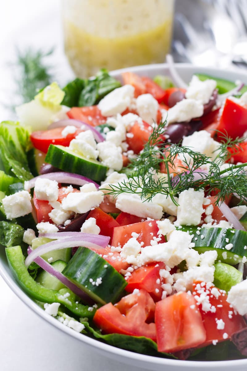 Close up of Greek Salad on white bowl and a mason jar with dressing