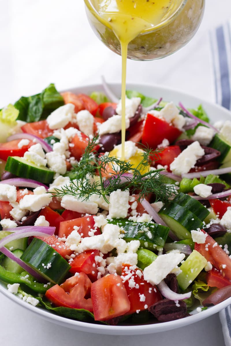 Greek dressing being poured into a a bowl of Greek Salad