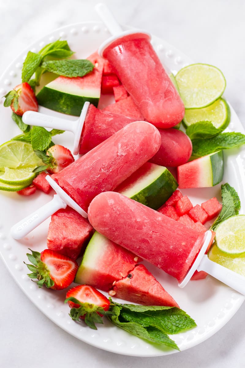 White oval plate with watermelon popsicles, mint, sliced watermelon and limes