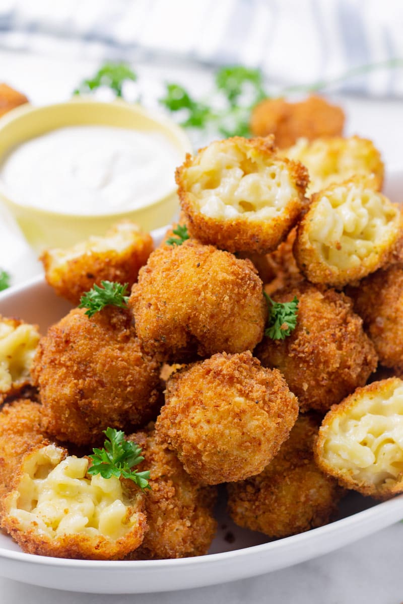 A pile of mac and cheese appetizers with ranch ranch sauce in the back