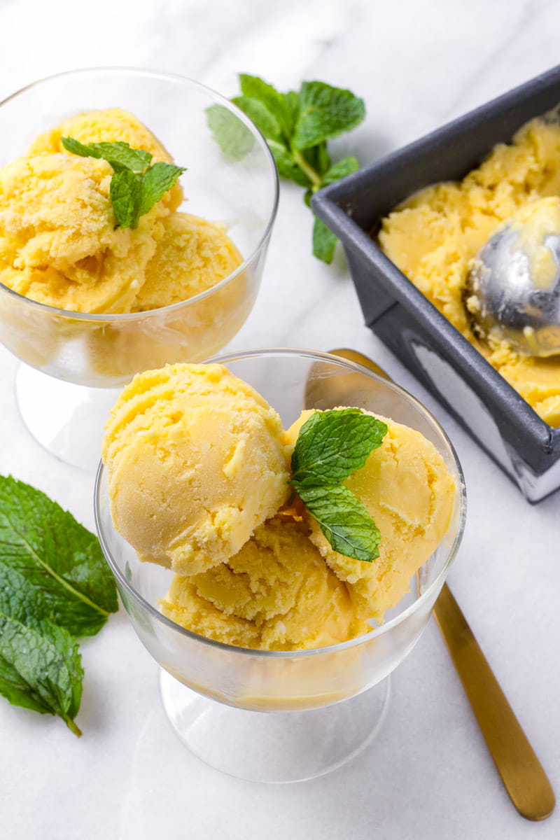 Two bowls with yellow ice cream and a gold color spoon