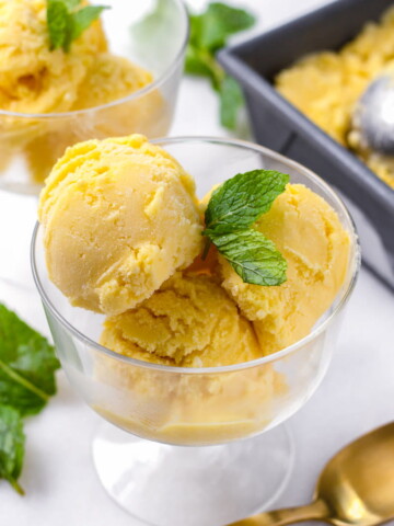 A glass bowl with three scoops of mango ice cream and mint garnish