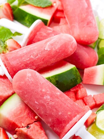 Four red watermelon popsicles on a bed of watermelon and limes