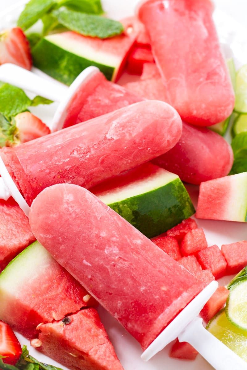 Four red watermelon ice pop treats on a bed of watermelon and limes