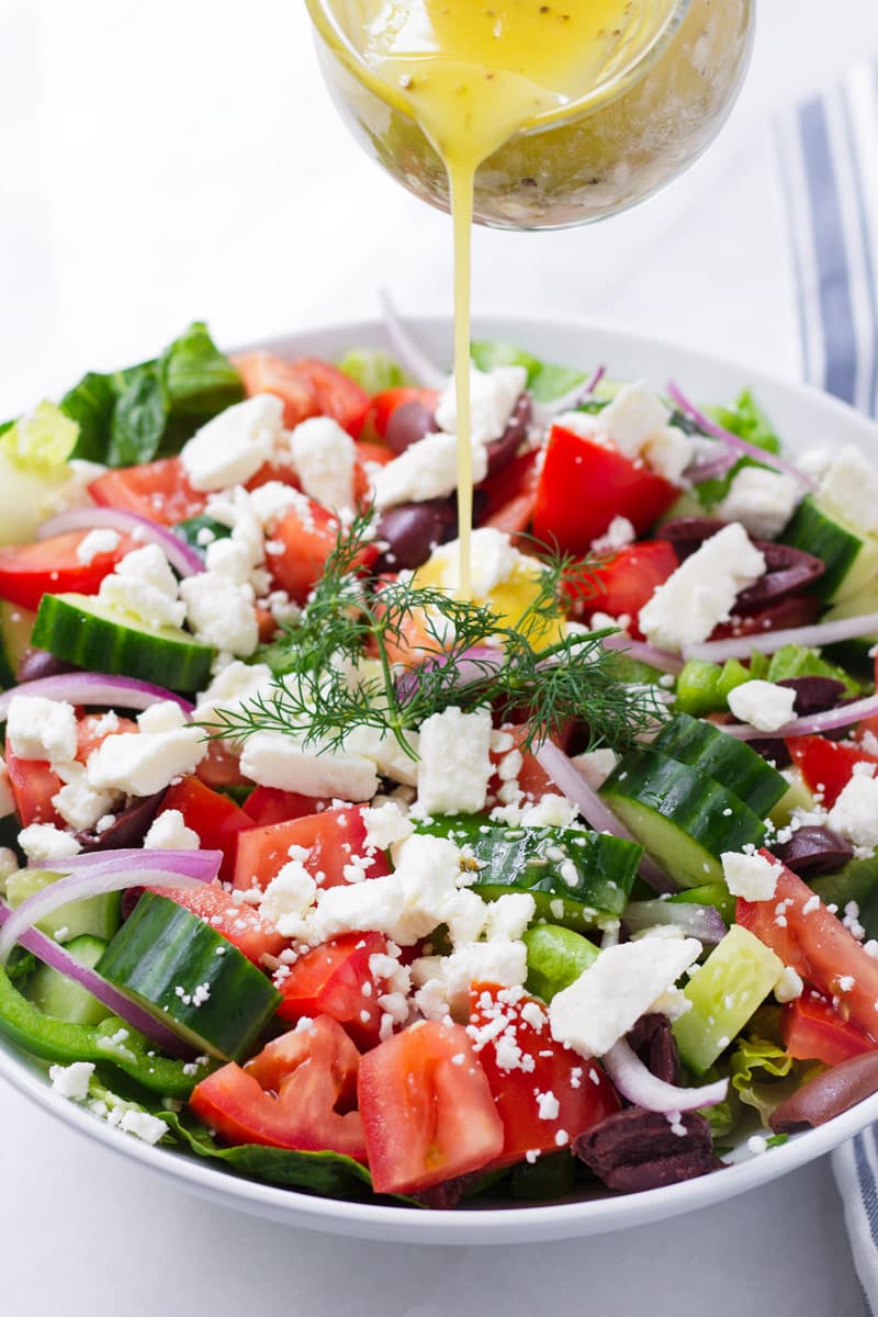 Greek yellow dressing being poured onto a plate of fresh salad