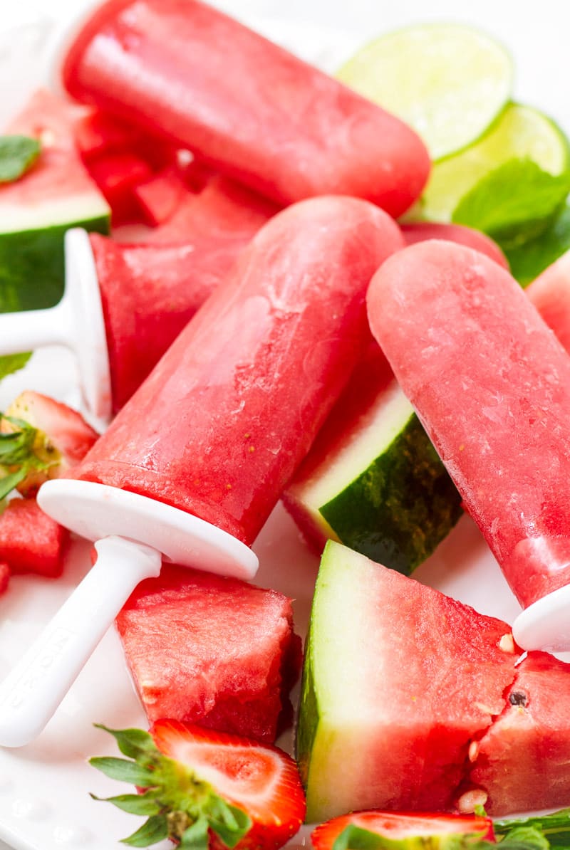 Homemade watermelon strawberry ice pops resting on cut up watermelon