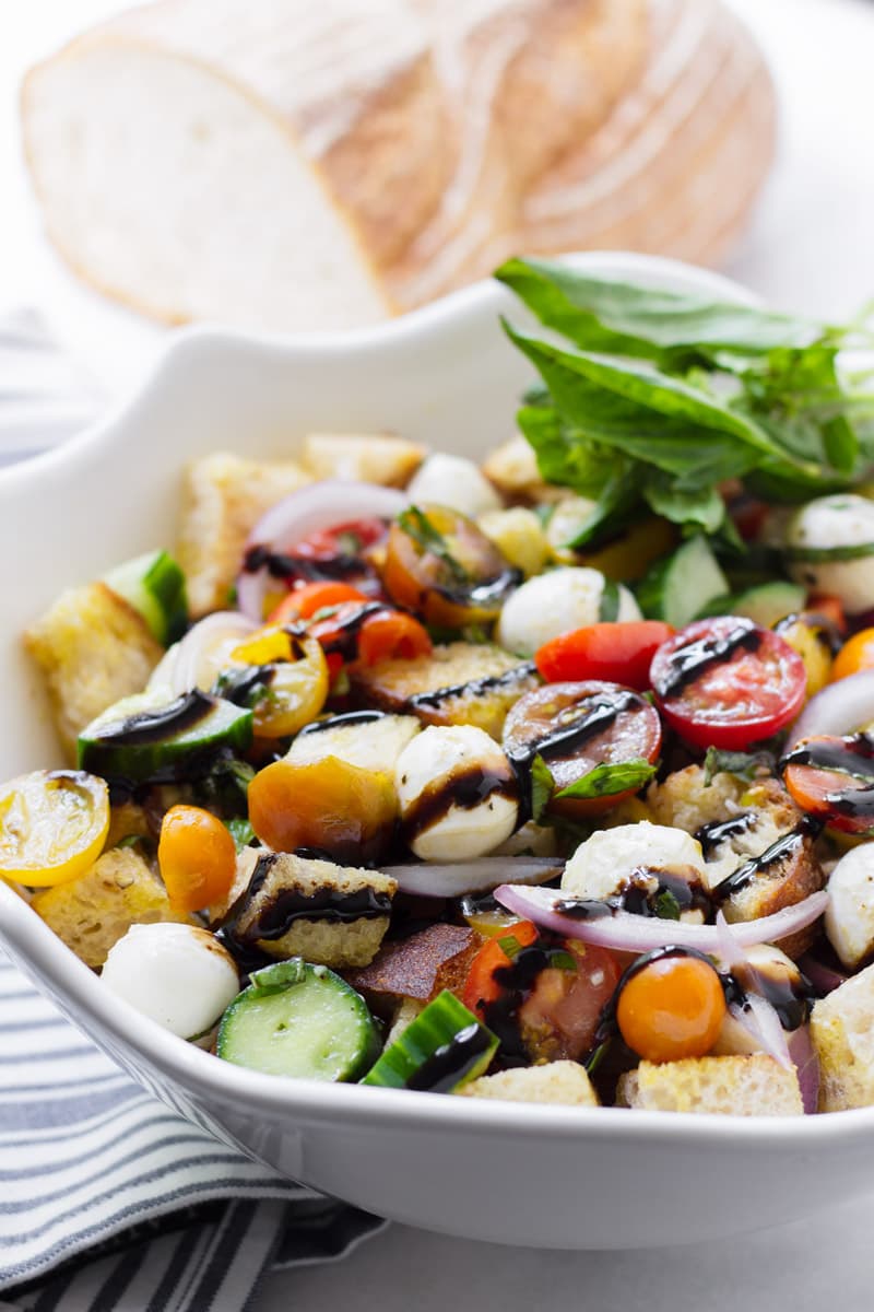 Side view of panzanella salad in a large white bowl and bread in the backgroun