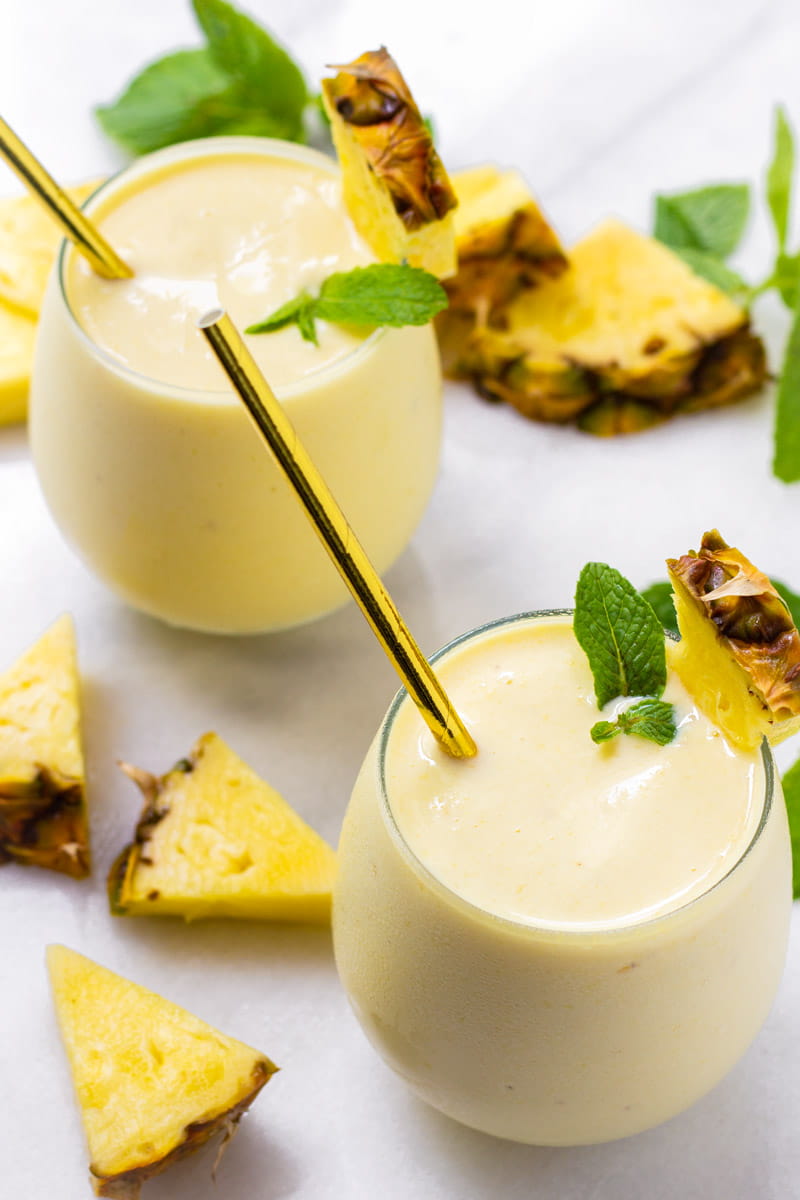 Two glasses with pineapple banana smoothie with pineapple slices and mint garnish