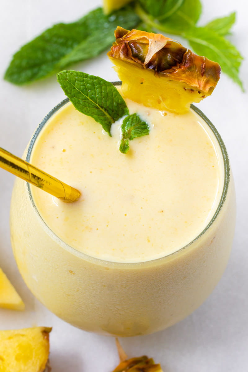Pineapple smoothie with a golden straw and mint and pineapple garnish