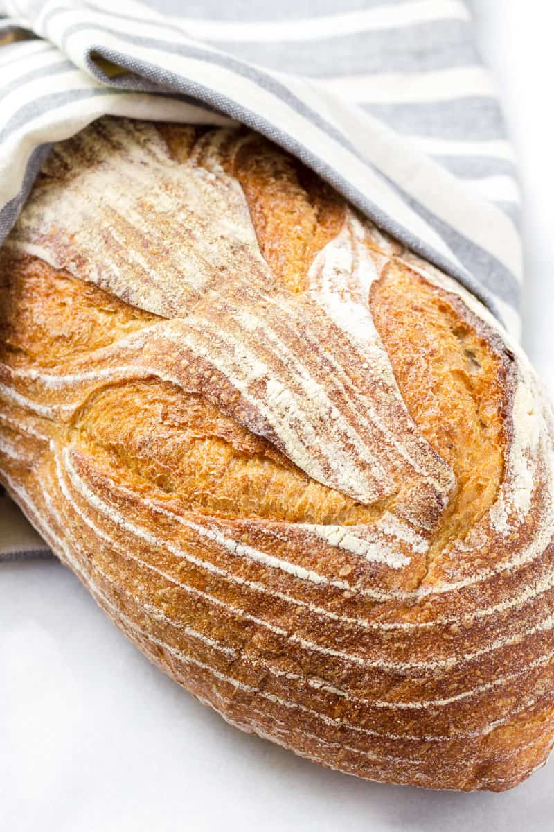 Large loaf of rustic bread partially covered with a kitchen towel