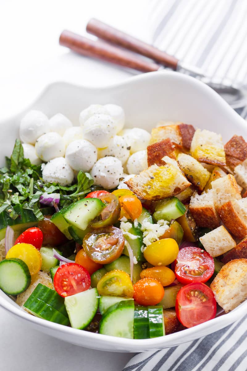 Large bowl with cucumbers, tomatoes, bread cubes, mozzarella, and basil