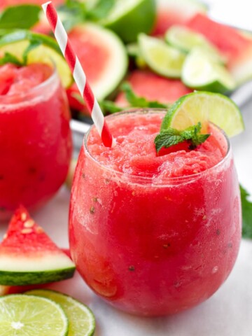 Red watermelon slush with red and white paper straw, plus lime and mint garnish