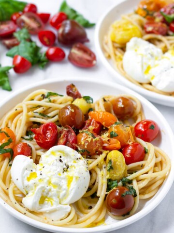 Two plates with fresh tomato sauce pasta and fresh burrata drizzled with olive oil