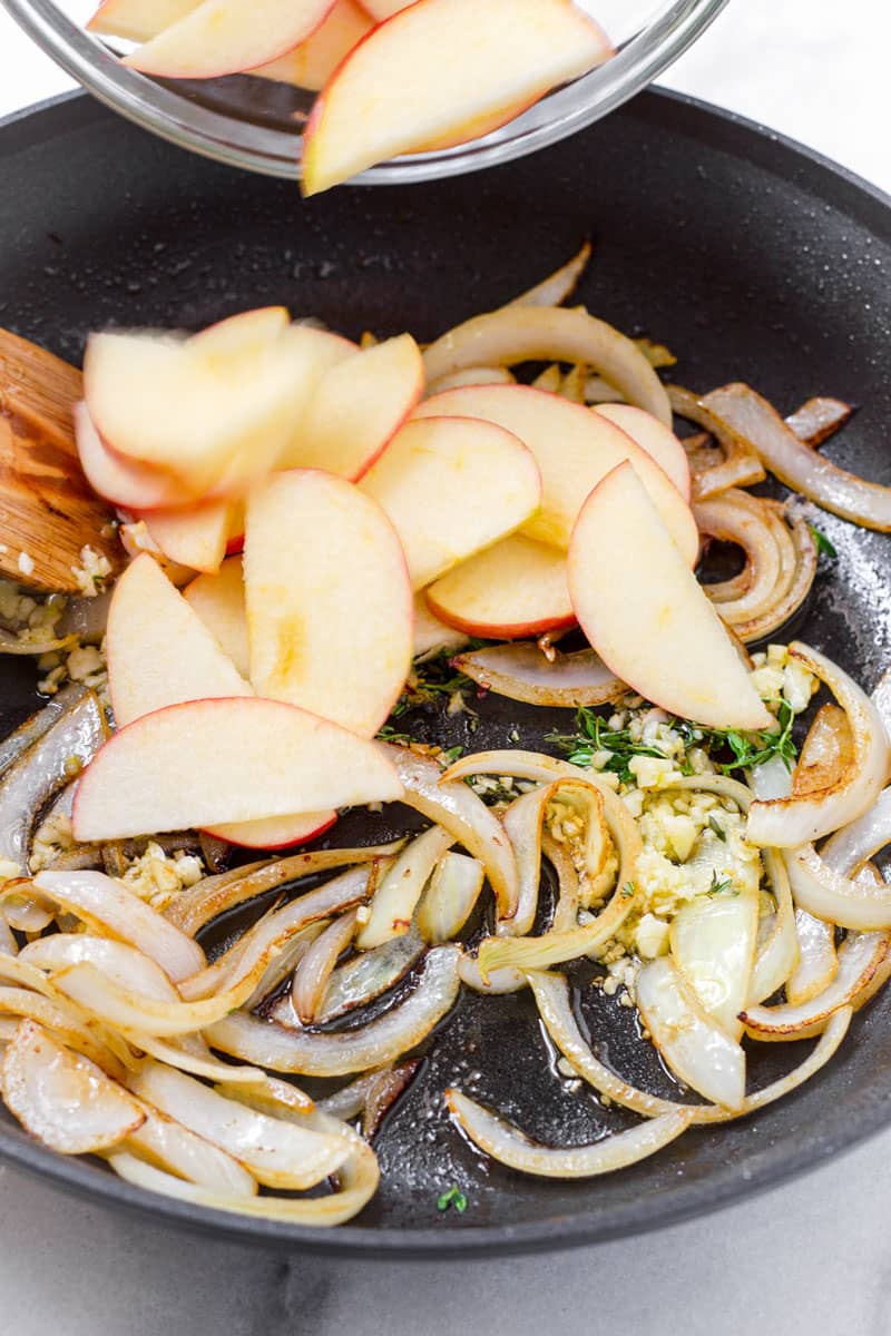 raw sliced apples being poured onto a skillet along with onions