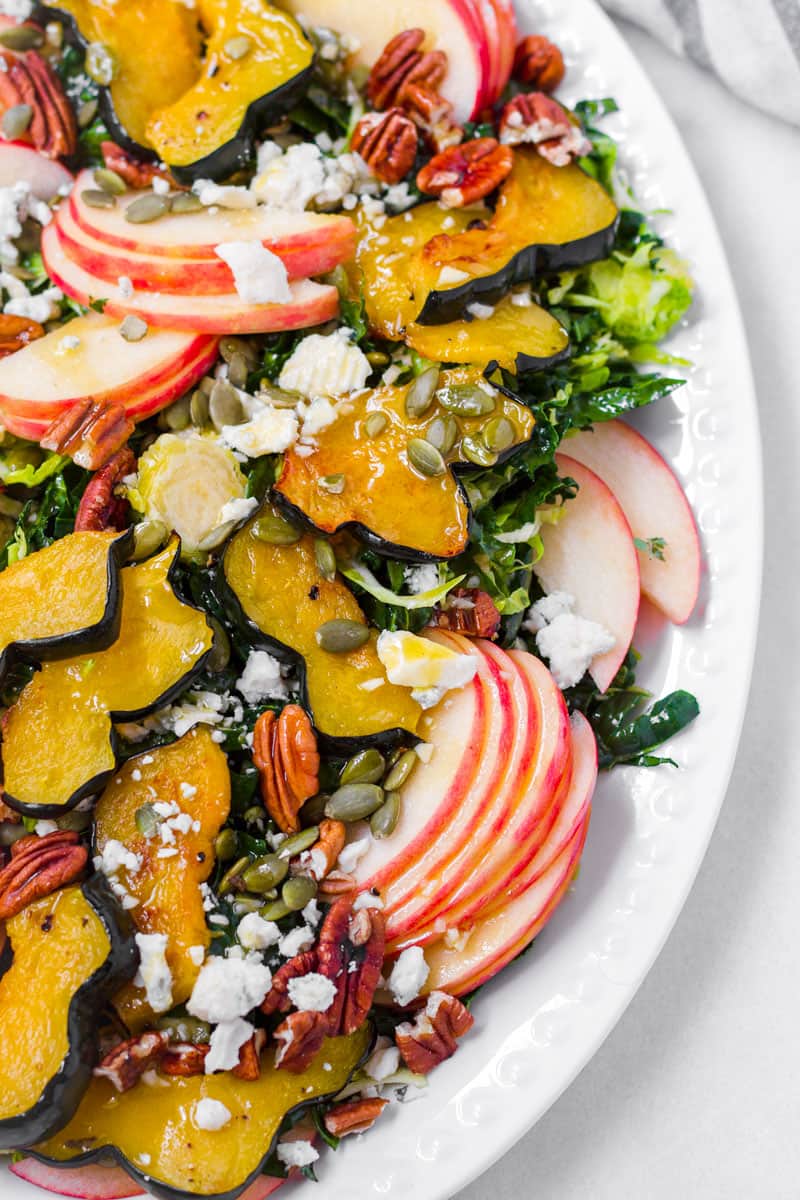 Half view of a fall themed salad platter made of apples, roasted acorn squash, kale, cheese, and nuts