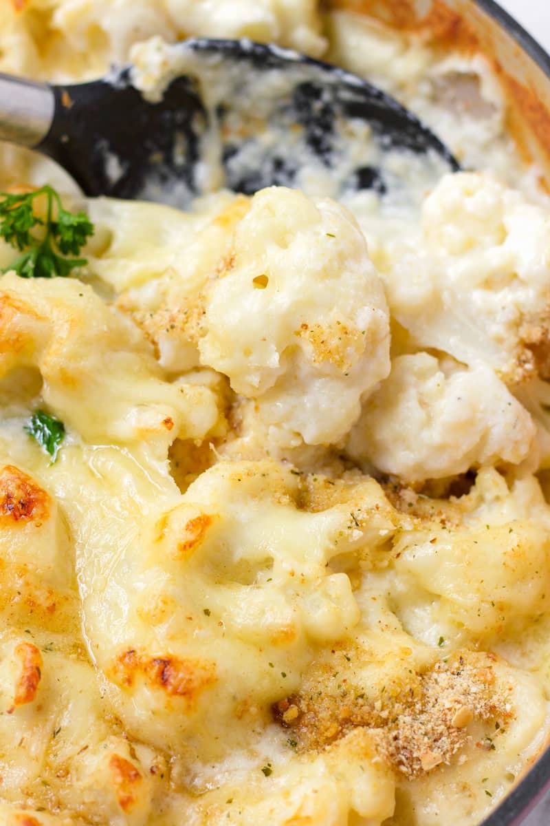 a spoon scooping out cauliflower with cheese sauce