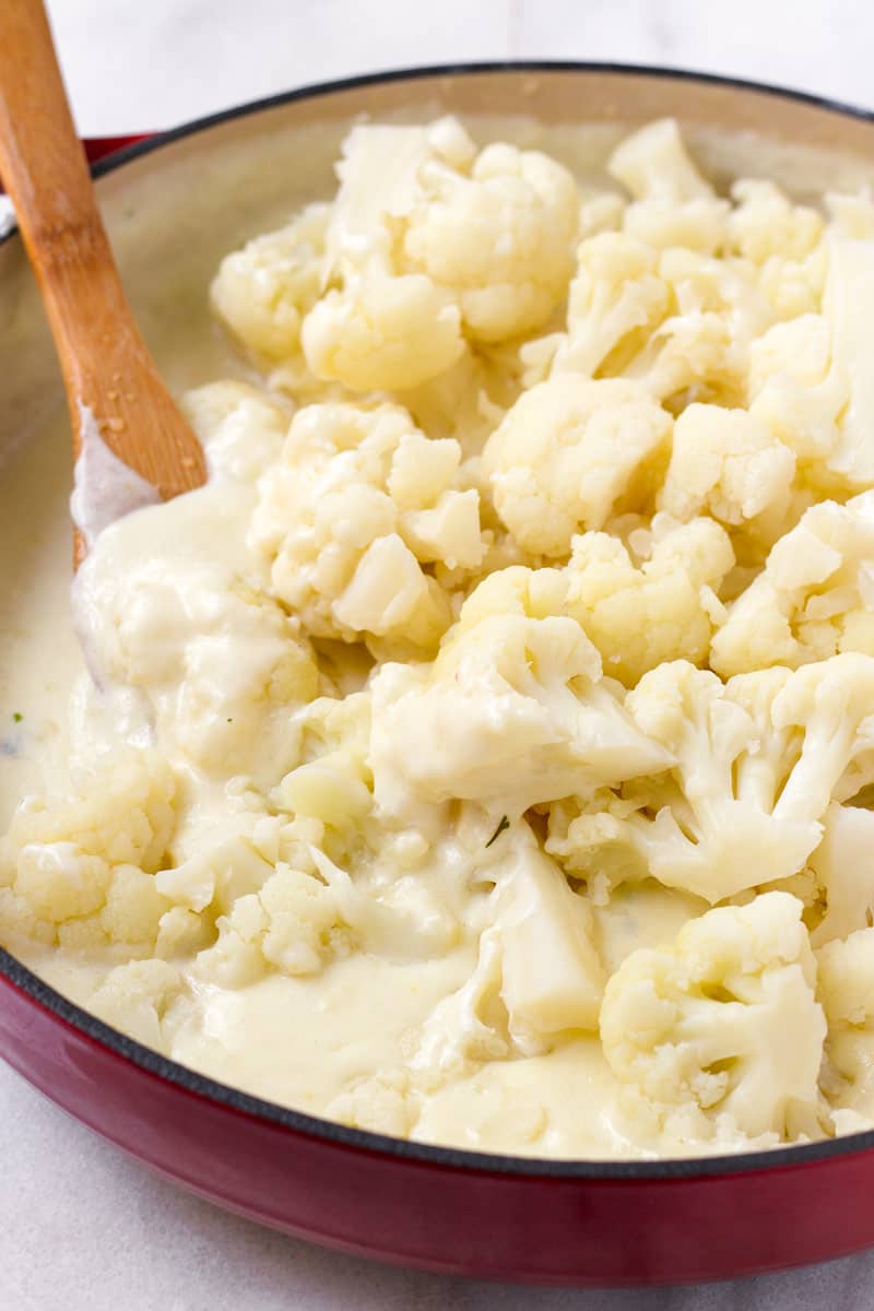 Steamed cauliflower being tossed with a white cheese sauce in a pot