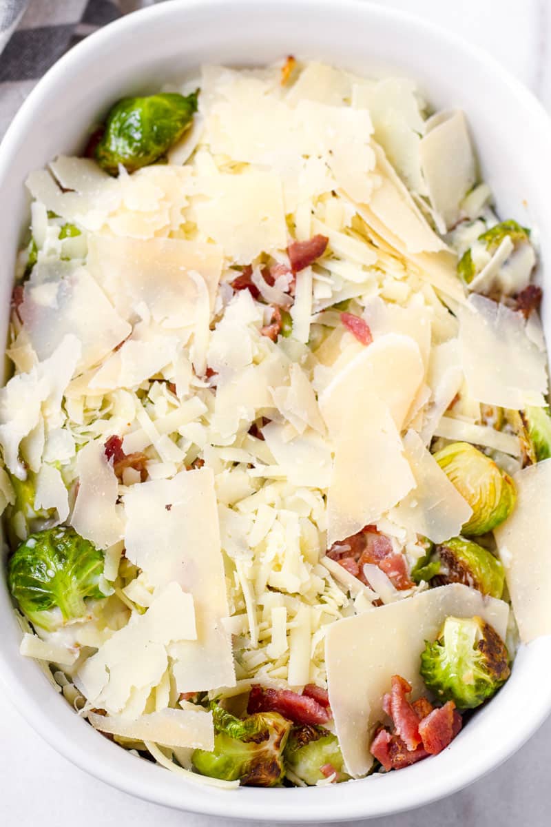 Oval shaped baking dish with brussels sprouts and topped with cheese before being baked