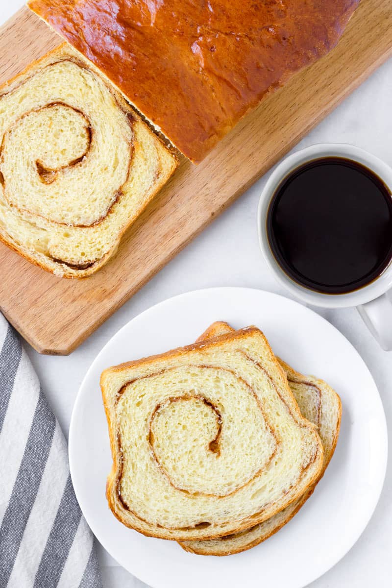 Top view of sliced cinnamon loaf on a wooden board with a cup of coffee and more slices