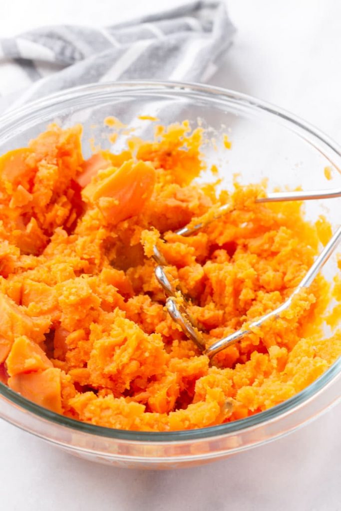 a masher in a glass bowl mashing cooked sweet potatoes