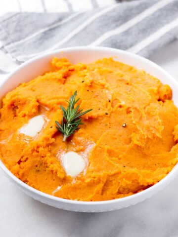 white bowl with prepared mashed sweet potatoes with melty butter and rosemary on top
