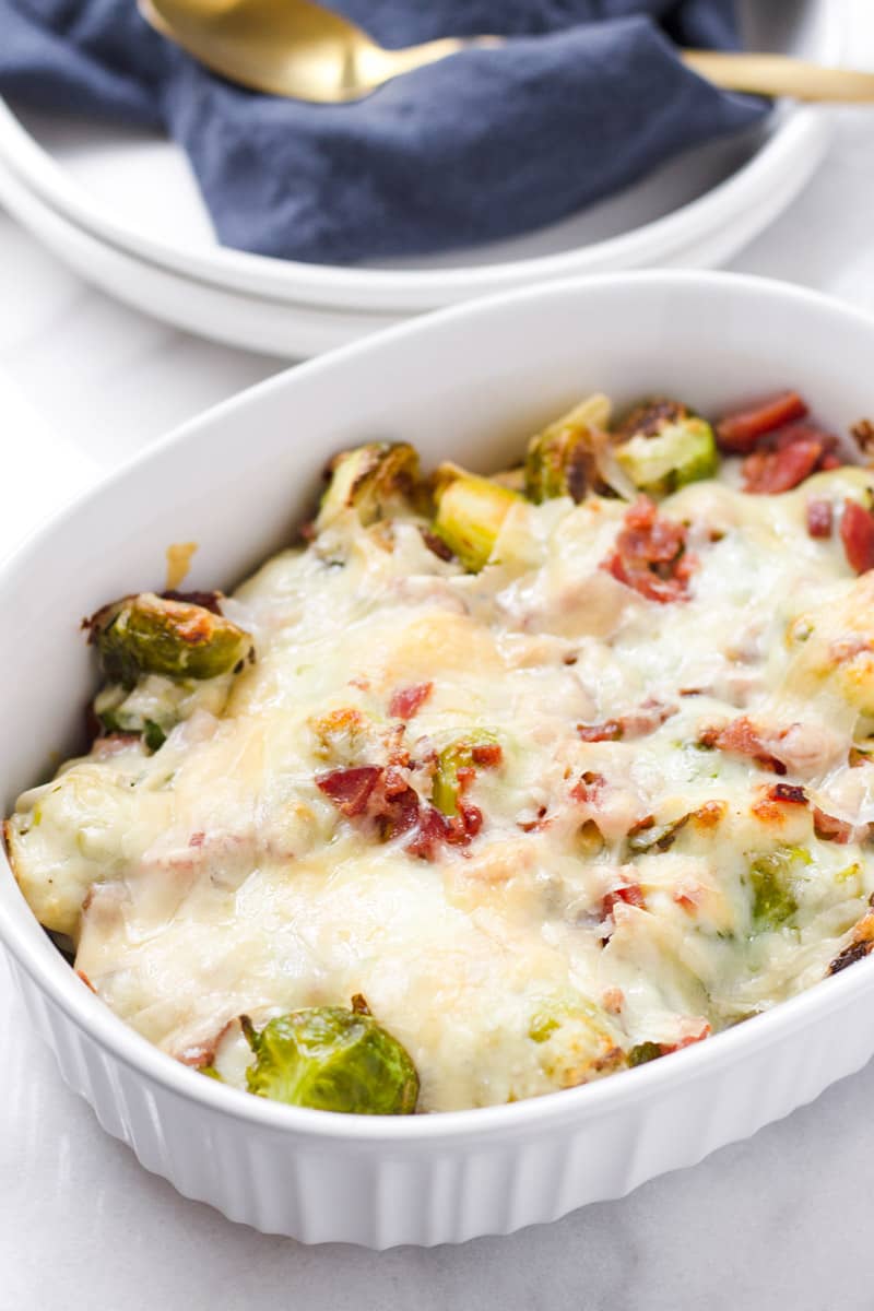 Baked brussels sprouts au gratin with bacon served in a white oval baking dish