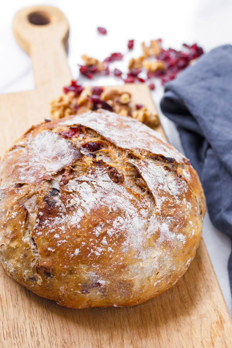 baked round loaf of artisan cranberry bread on a wooden board next to napkin