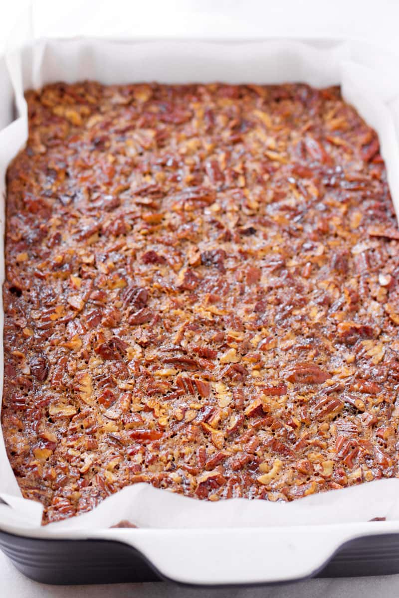 A 9 by 13 baking pan with baked pecan pie bar on parchment paper