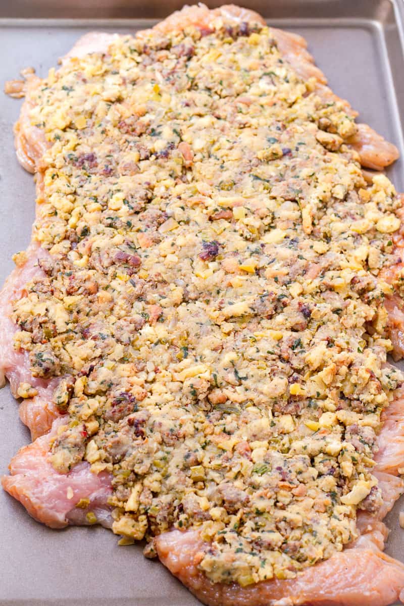 Flat turkey breast with stuffing spread on top, sitting on a sheet pan