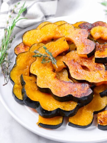 maple roasted acorn squash slices piled up on plate and with rosemary garnish