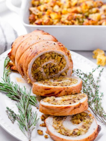 cooked roasted turkey roll with three slices on an oval plate, garnished with thyme and rosemary