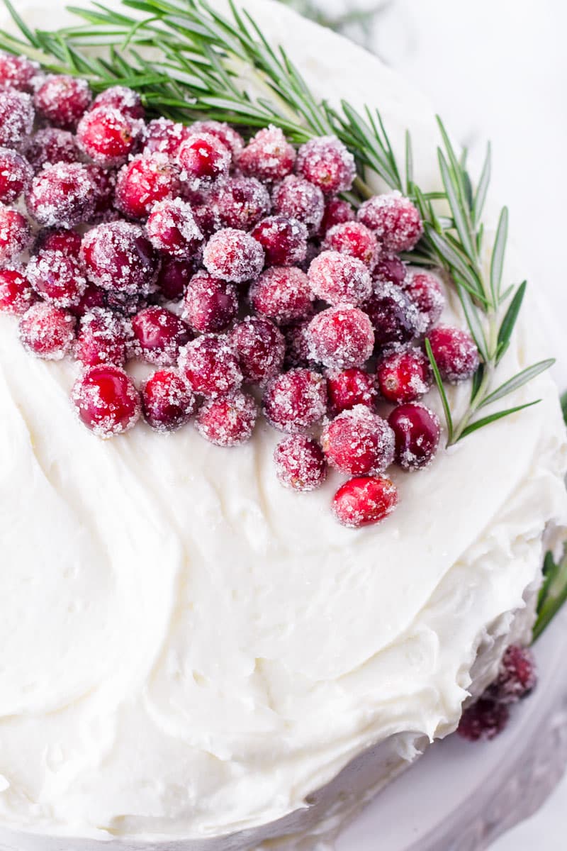 White frosted cake decorated with sugared cranberries and rosemary