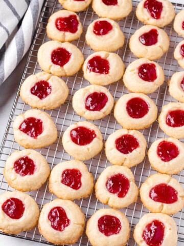 About 28 raspberry butter cookies lined up on a cooling rack