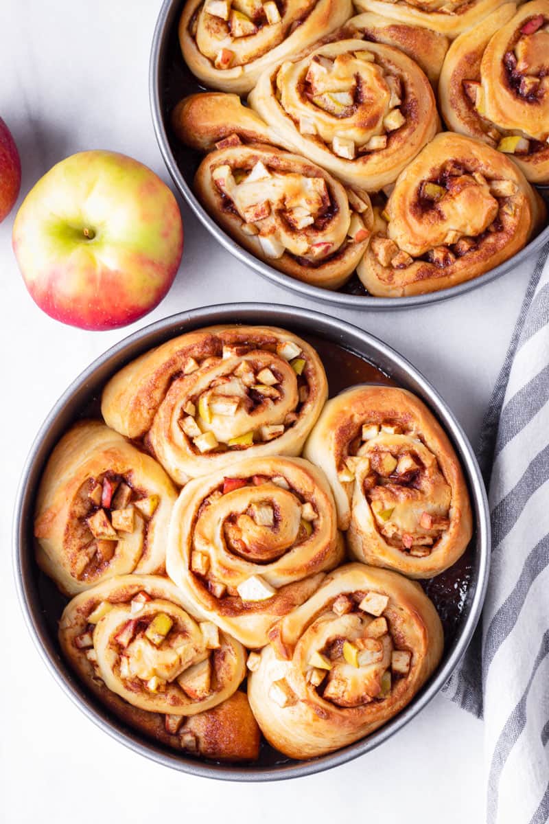 Two round pans with apple cinnamon rolls, plus apples and napkins on the side