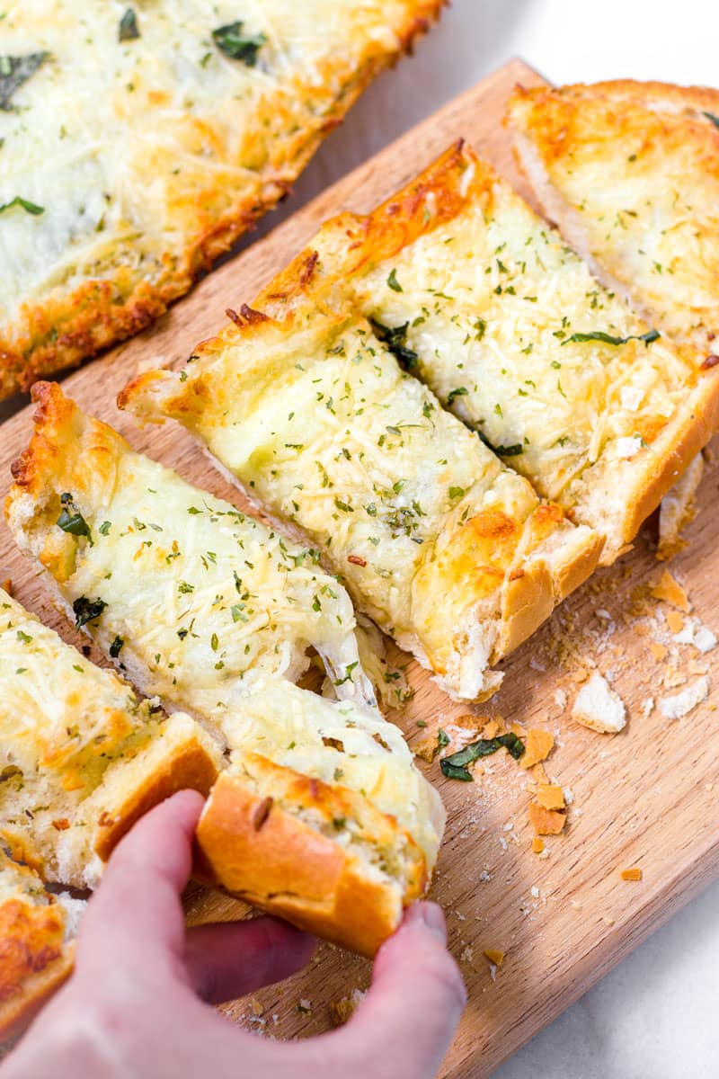 a hand pulling a slice of cheese garlic bread