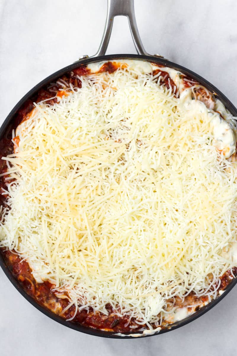Deep skillet topped with shredded cheese and sauce