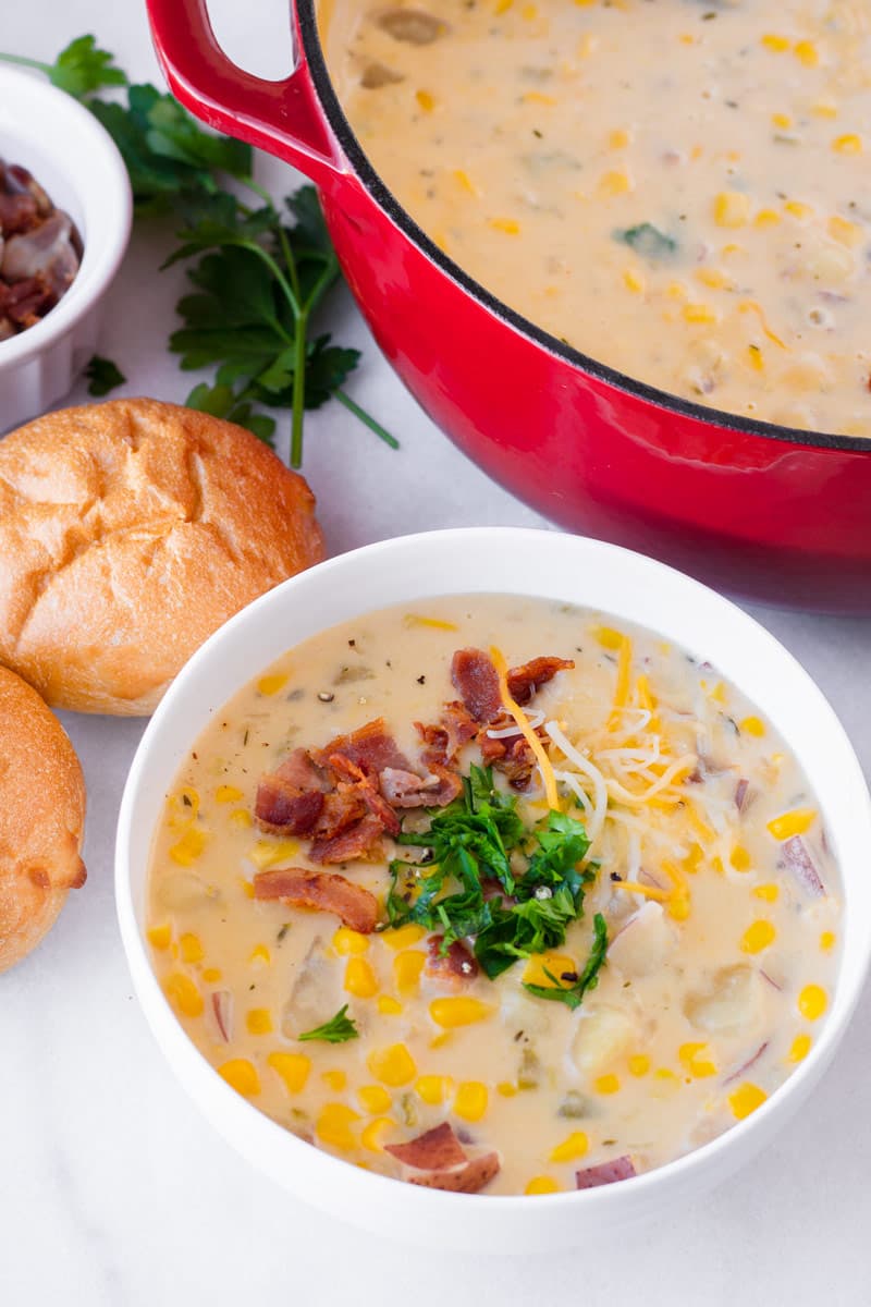 A red Dutch oven and a white ceramic bowl with potato corn chowder