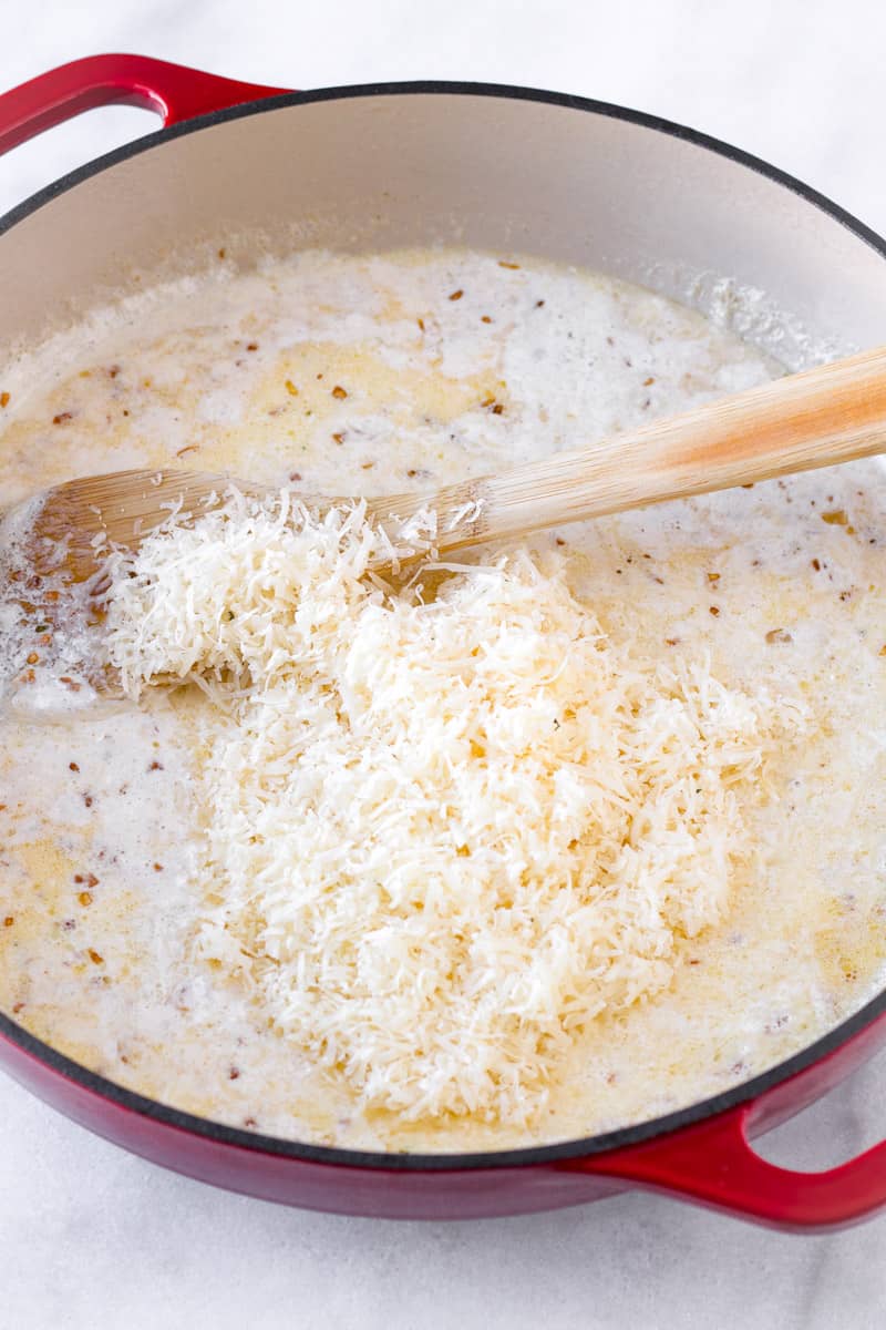 grated parmesan cheese with heavy cream in a red Dutch oven and a wooden spoon
