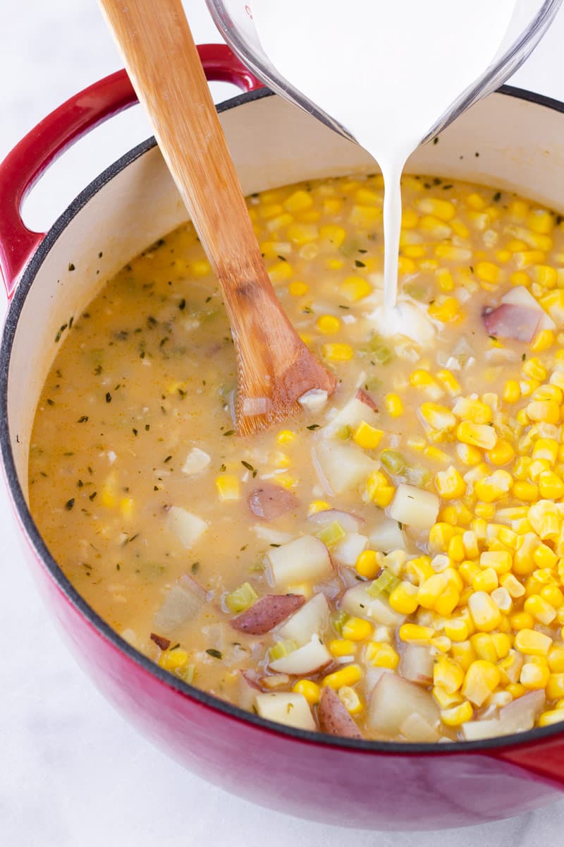 heavy cream being poured into a pot with corn, broth, and vegetables